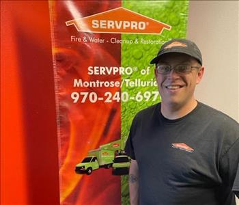 Male smiling in black SERVPRO teeshirt and hat in front of banner