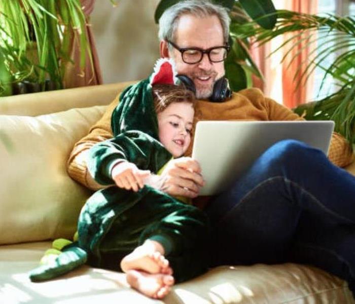 A child and man sitting on a couch watching a tablet.